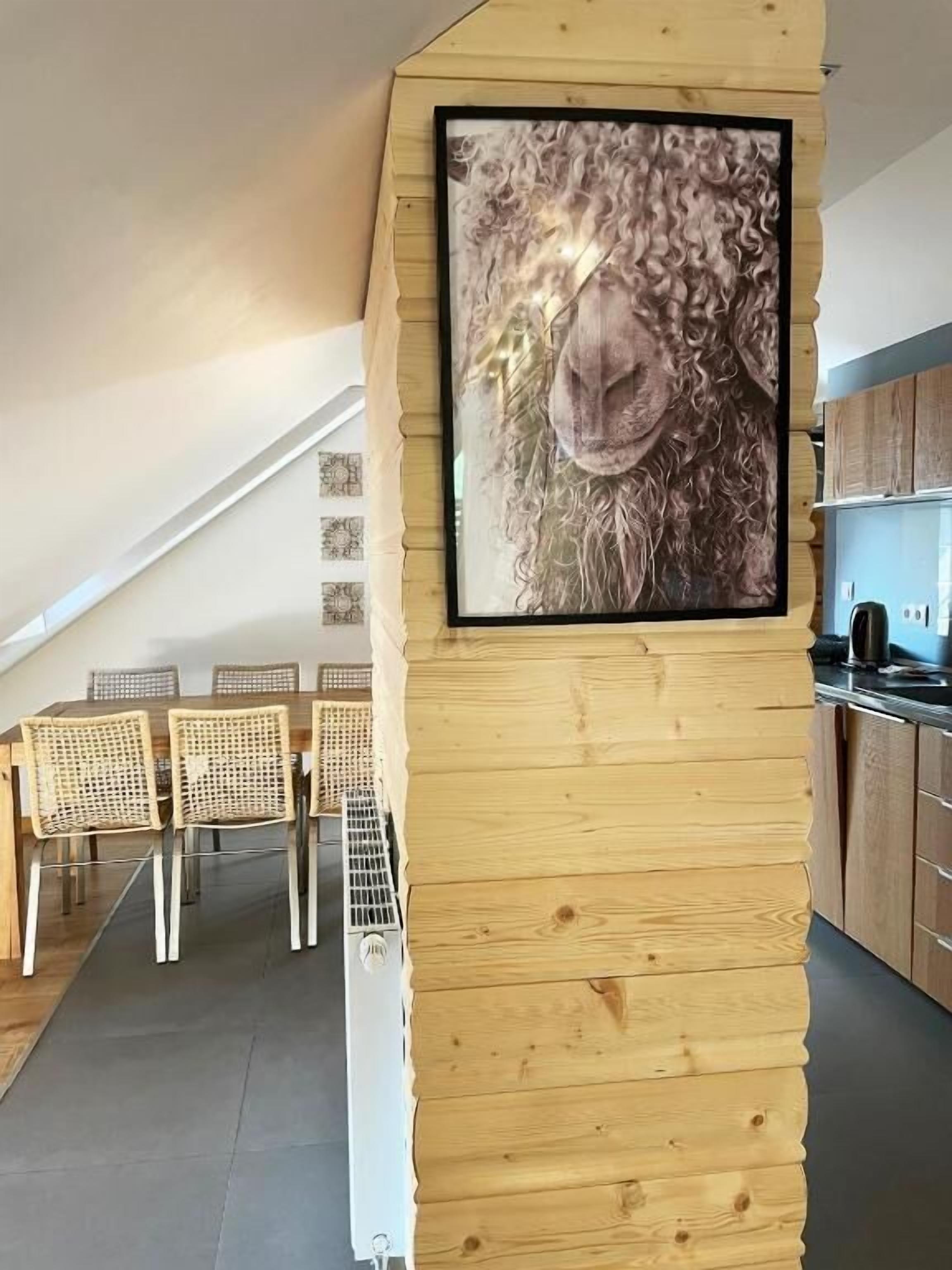 A modern kitchen with wooden cabinetry, a dining area with wicker chairs, and a framed artwork of a sheep's face.
