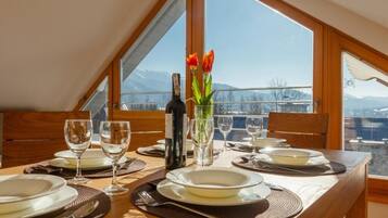 A dining table set for four with a bottle of wine, two tulips, and a view of mountains through large windows.