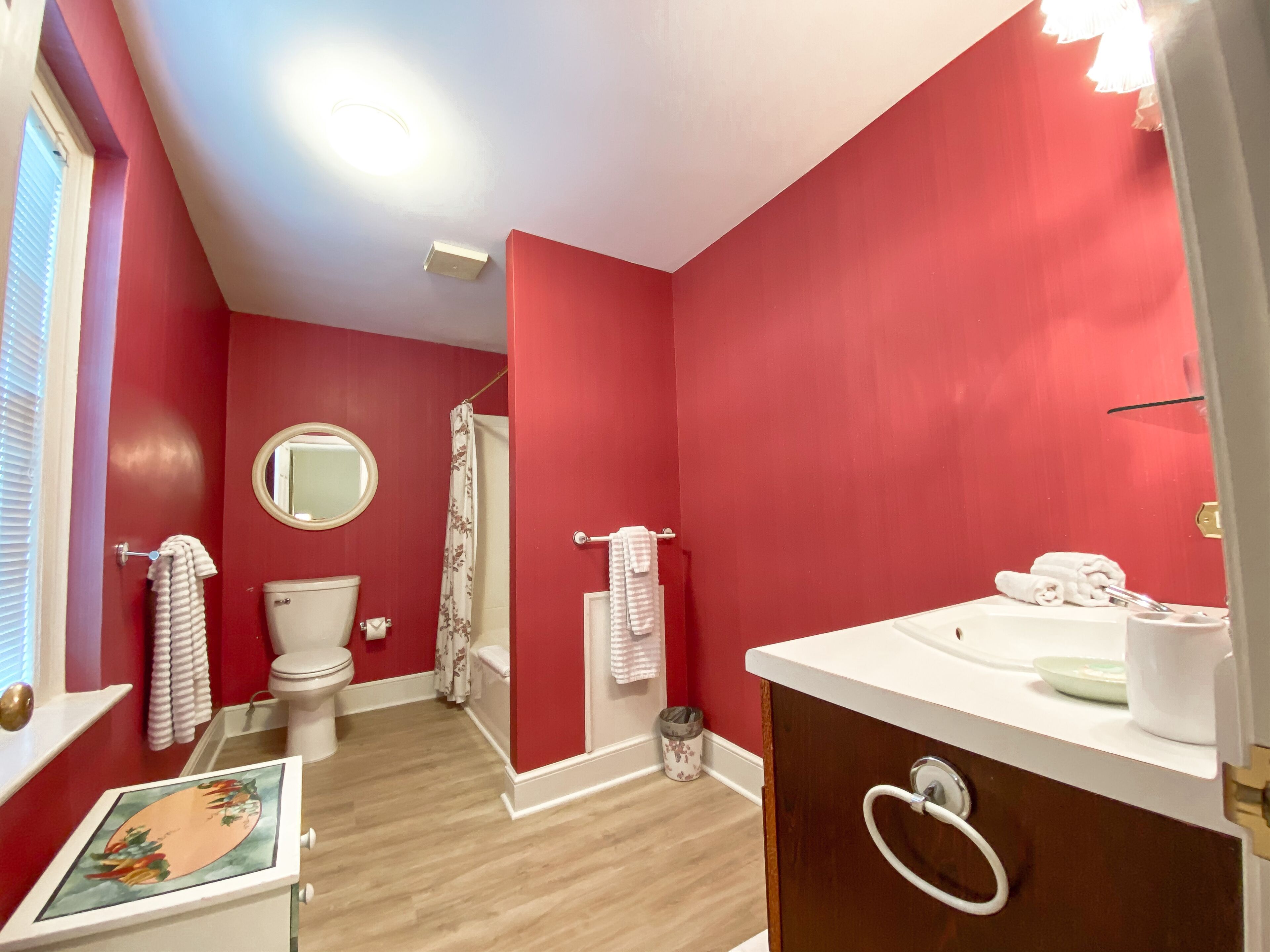 A bathroom with red walls, a white toilet, a sink with a mirror, and a shower curtain.