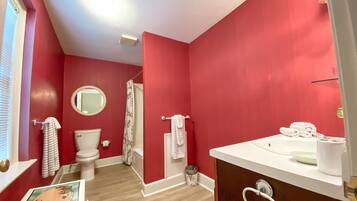 Un baño con paredes rojas, inodoro blanco, lavabo con espejo y cortina de ducha.