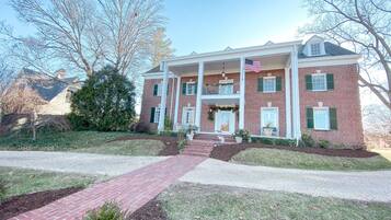 A two-story brick house with a front porch, a flag, and a well-maintained lawn.