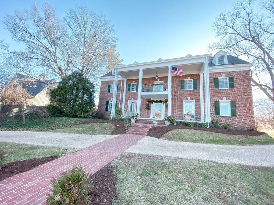 A two-story brick house with a front porch, a flag, and a well-maintained lawn.