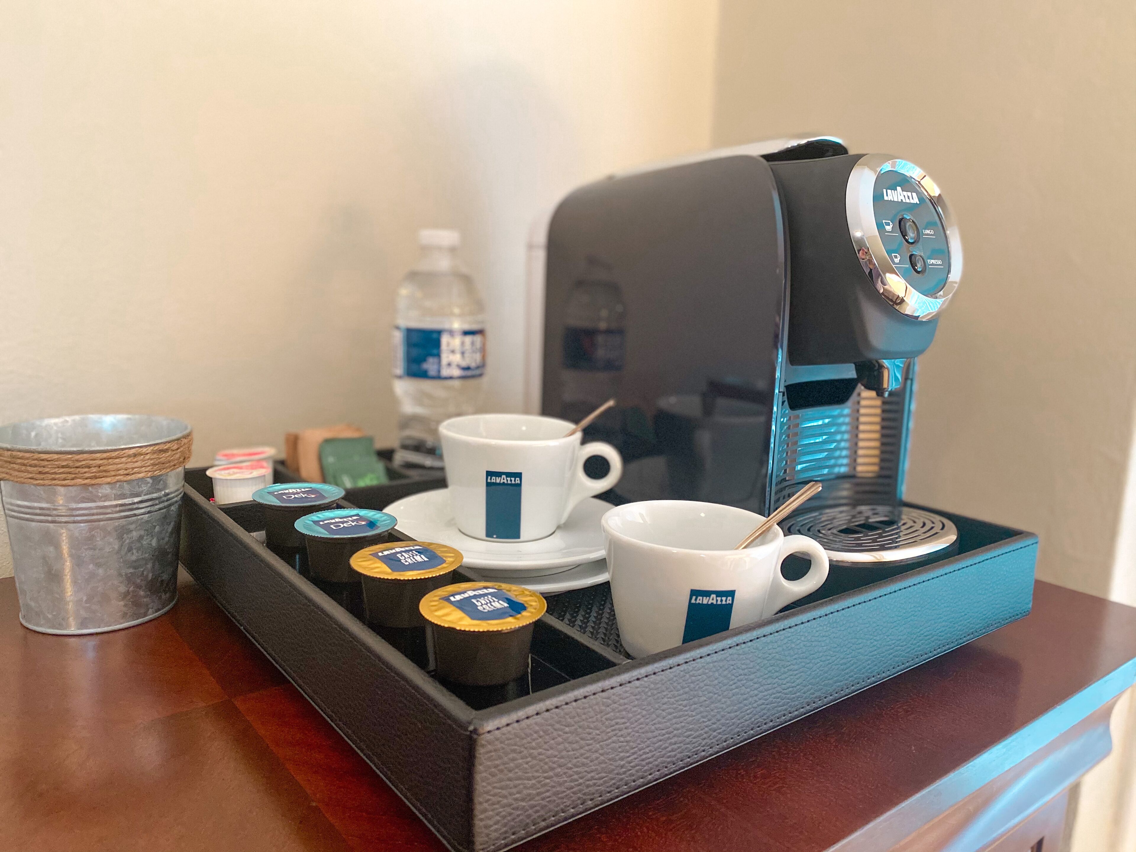 A coffee station with a coffee machine, cups, and coffee pods on a tray.