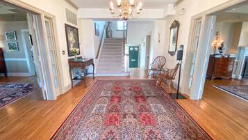 A spacious hallway with a large patterned rug, wooden flooring, a chandelier, and a staircase leading to another room.