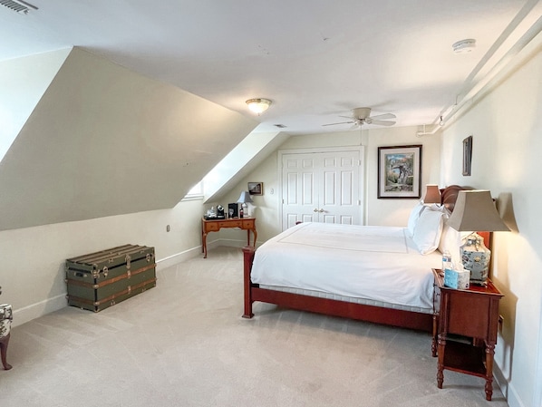 A bedroom with a sloped ceiling, a bed, a nightstand, a lamp, a dresser, and a suitcase.