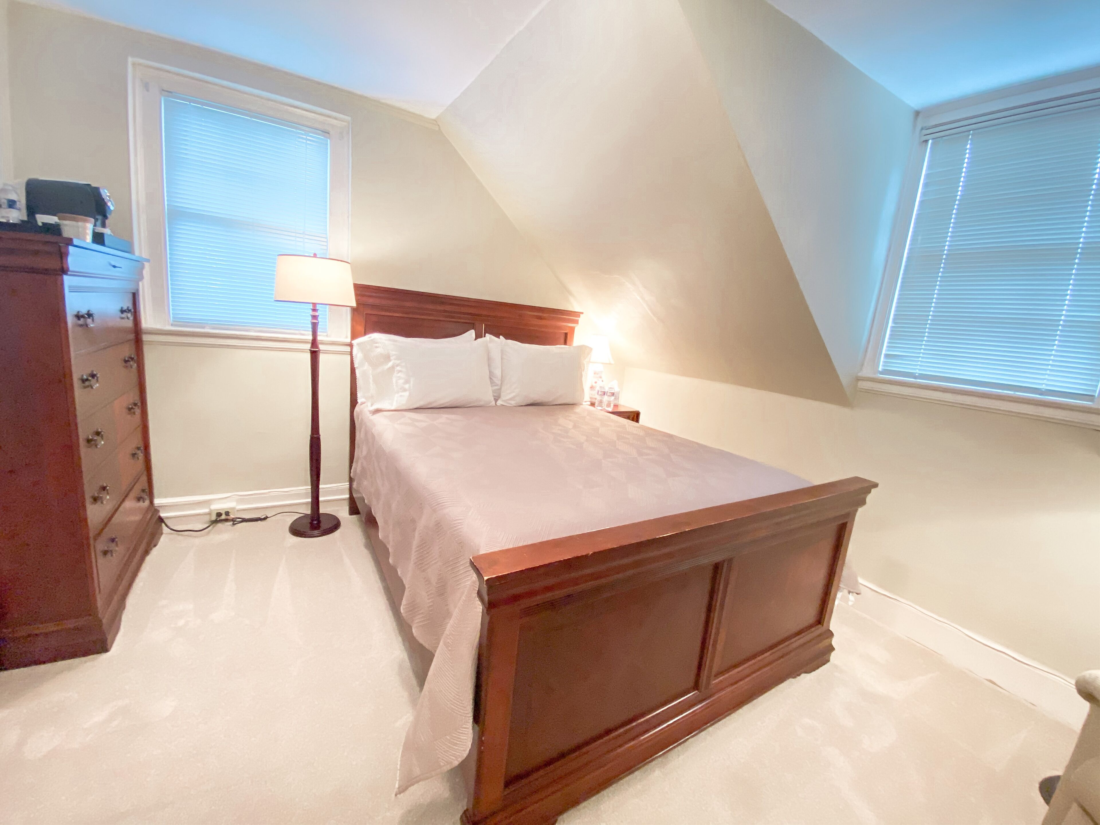 Un dormitorio con una cama de madera, un aparador, una lámpara y una ventana con persianas.