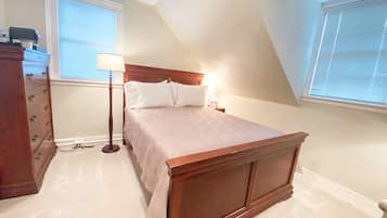 Un dormitorio con una cama de madera, un aparador, una lámpara y una ventana con persianas.
