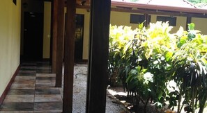 A corridor with tiled flooring leading to a covered outdoor area with a garden. - Hotel Flor de Itabo (Sardinal)