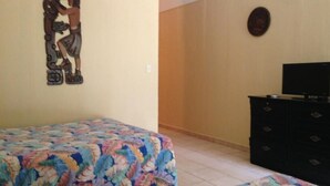 A bedroom with a floral bedspread, a dresser with a television on top, and a wall decoration. - Hotel Flor de Itabo (Sardinal)