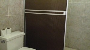 A bathroom with a toilet, two rolls of toilet paper, and a shower stall with a brown shower curtain. - Hotel Flor de Itabo (Sardinal)