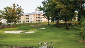 Un campo de golf con búnkeres, un puente de madera y un edificio de varios pisos al fondo.