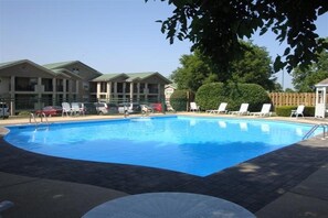 A swimming pool with lounge chairs, a covered area, and a building with a green roof in the background.