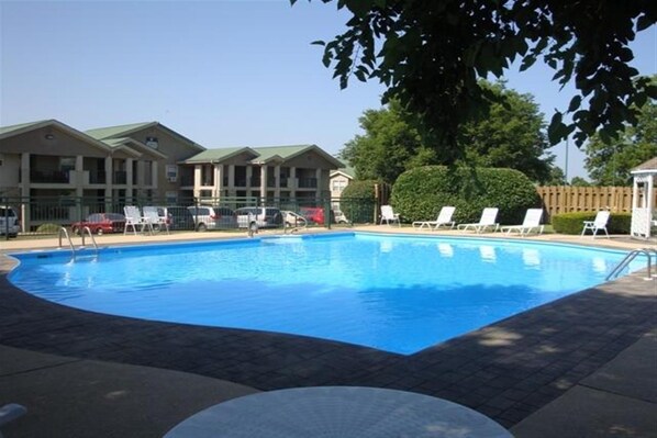 A swimming pool with lounge chairs, a covered area, and a building with a green roof in the background.