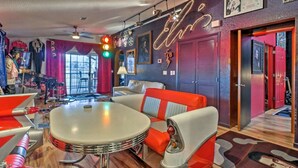 Habitación de estilo retro con una mesa redonda, sillas anaranjadas y blancas, y un letrero de neón en la pared.