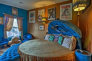 Un dormitorio con cama redonda, sillones tapizados en azul, un osito de peluche y carteles antiguos en la pared.