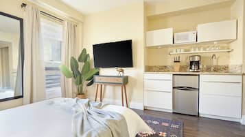 A hotel room with a bed, a television, a small kitchenette, and a large window.