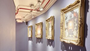 A hallway with a brick floor, white ceiling pipes, and a wall with framed pictures. - Kasa Gaslamp Quarter San Diego (San Diego)