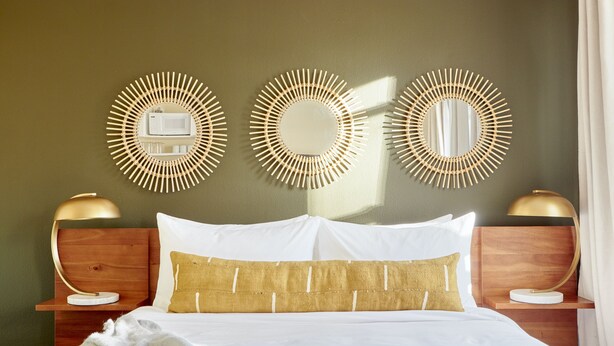 A neatly made bed with white and gold bedding, two bedside tables with lamps, and three wall-mounted mirrors. - Kasa Gaslamp Quarter San Diego (San Diego)