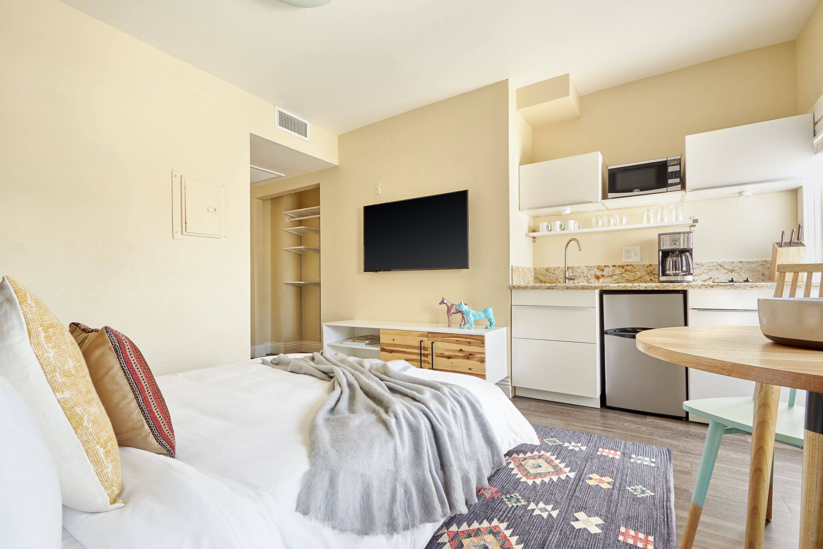 Een hotelkamer met een bed, een kitchenette met een magnetron, toaster en koffiezetapparaat, en een aan de muur bevestigde televisie.
