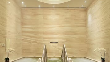 A modern spa with a large central bathtub, a staircase leading to it, and a decorative chandelier.