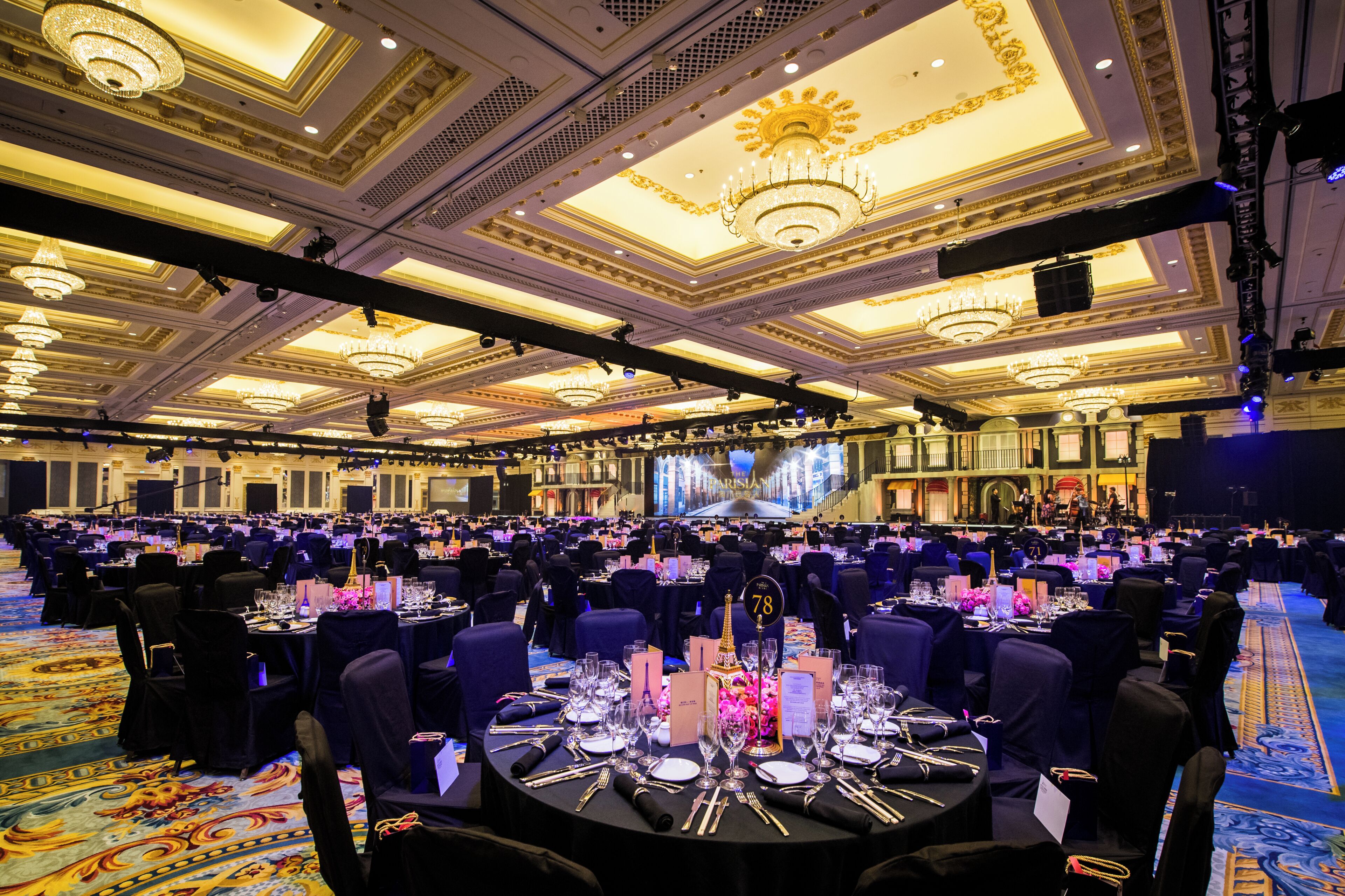 Un gran salón de banquetes con mesas redondas, candelabros y un escenario.