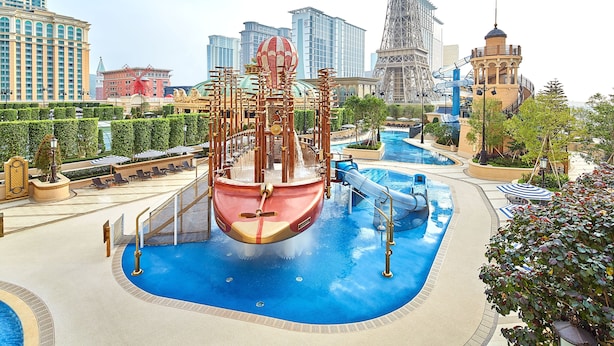 Un gran parque acuático cubierto con un área de juegos temática de barcos, una piscina y una vista de la Torre Eiffel al fondo.