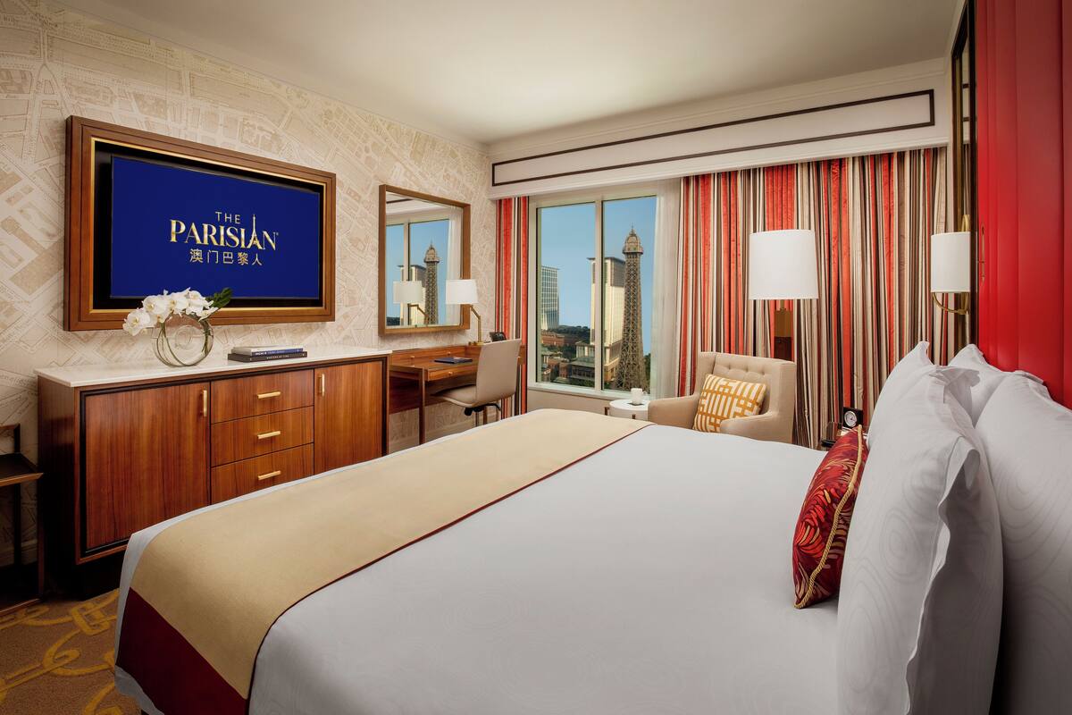 A hotel room with a large bed, a desk, a chair, a TV, and a view of the Eiffel Tower.