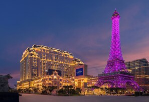 A large hotel with a prominent tower and the Eiffel Tower illuminated in purple. - The Parisian Macao (Cotai)