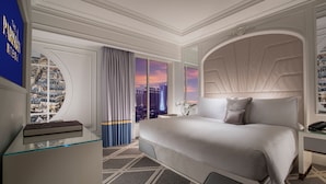 Una habitación de hotel moderna con una cama grande, un escritorio de vidrio, vistas a la ciudad y un cabecero decorativo.