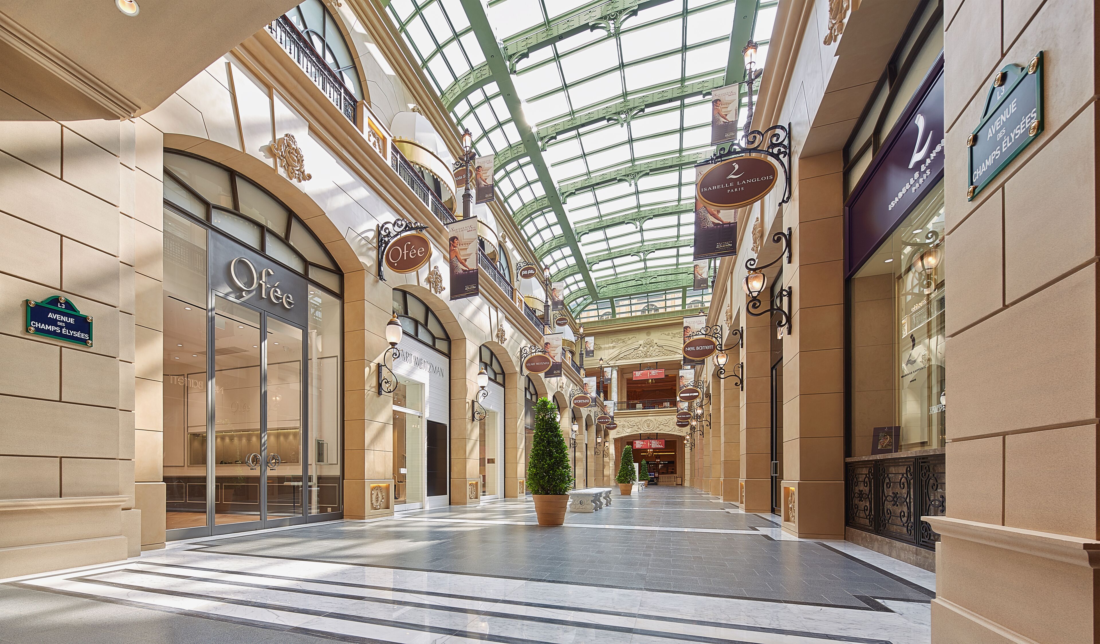 A spacious indoor shopping mall with a high glass ceiling, multiple levels, and various shops including a café.