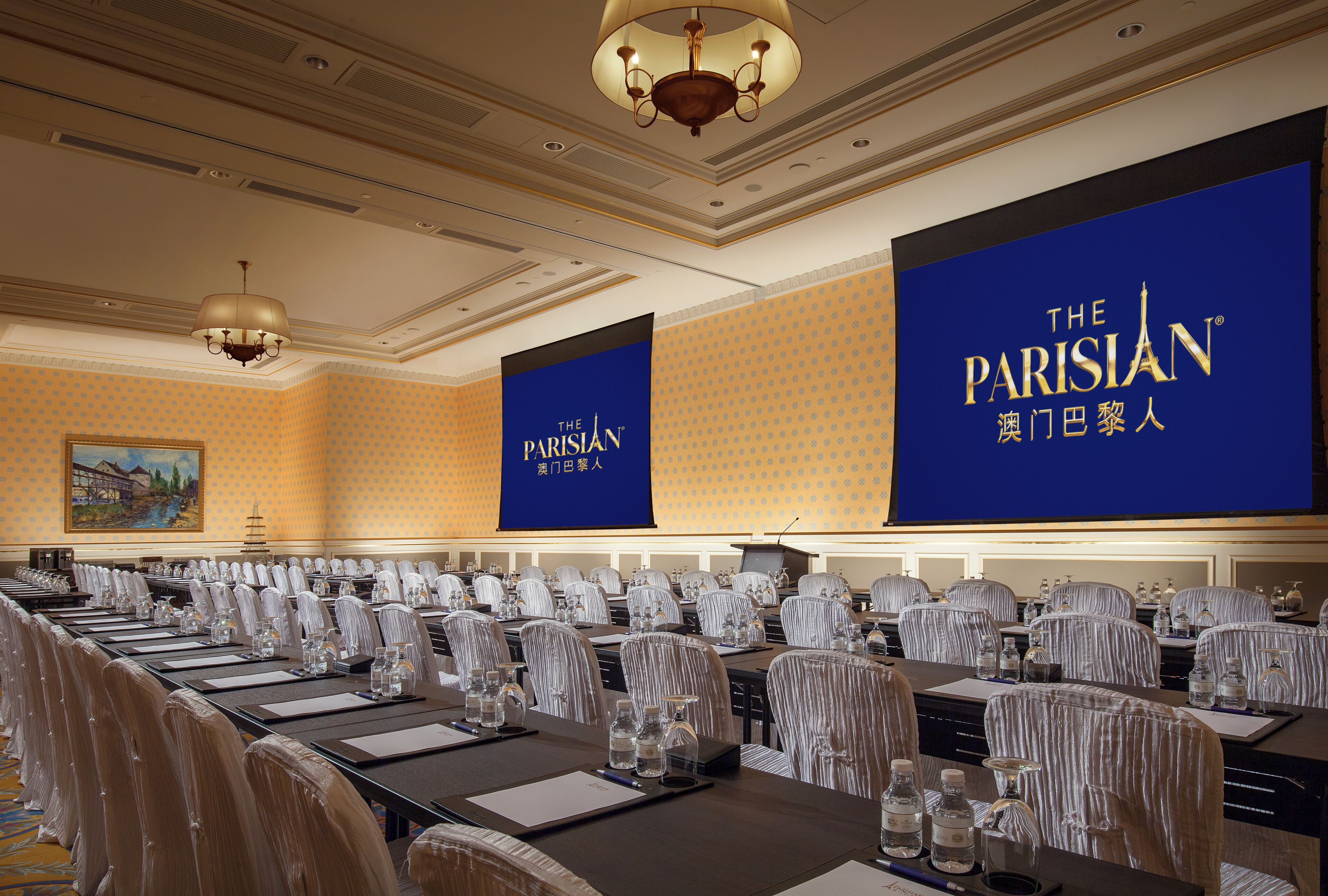 Un salón de conferencias con filas de mesas y sillas, grandes pancartas con el logotipo de 'The Parisian' y una araña.