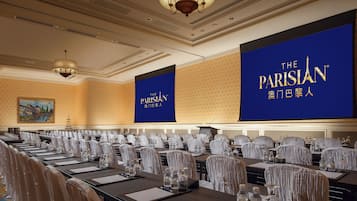 Un salón de conferencias con filas de mesas y sillas, grandes pancartas con el logotipo de 'The Parisian' y una araña.