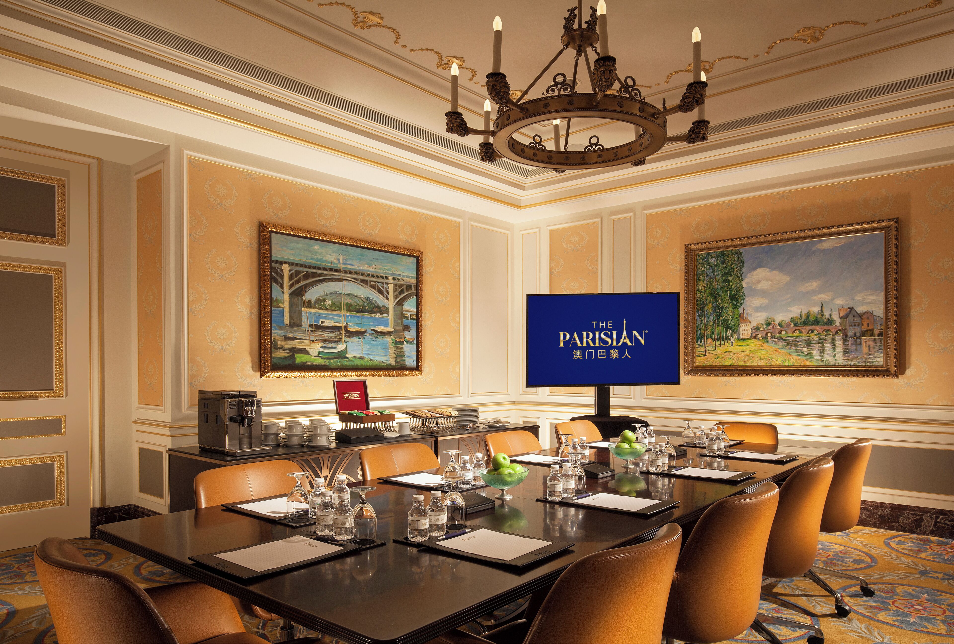 A conference room with a long table, chairs, a coffee station, and two paintings on the walls.