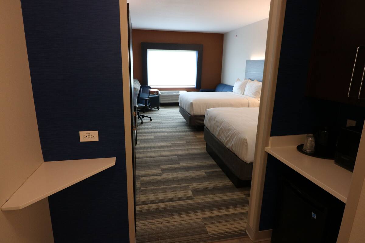 A hotel room with two beds, a desk, and a large window.