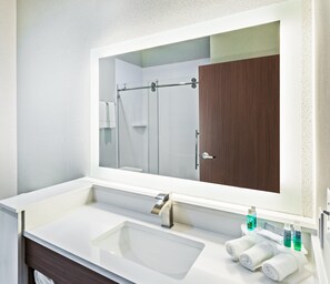 A modern bathroom with a large mirror, a white sink, and a wooden door.