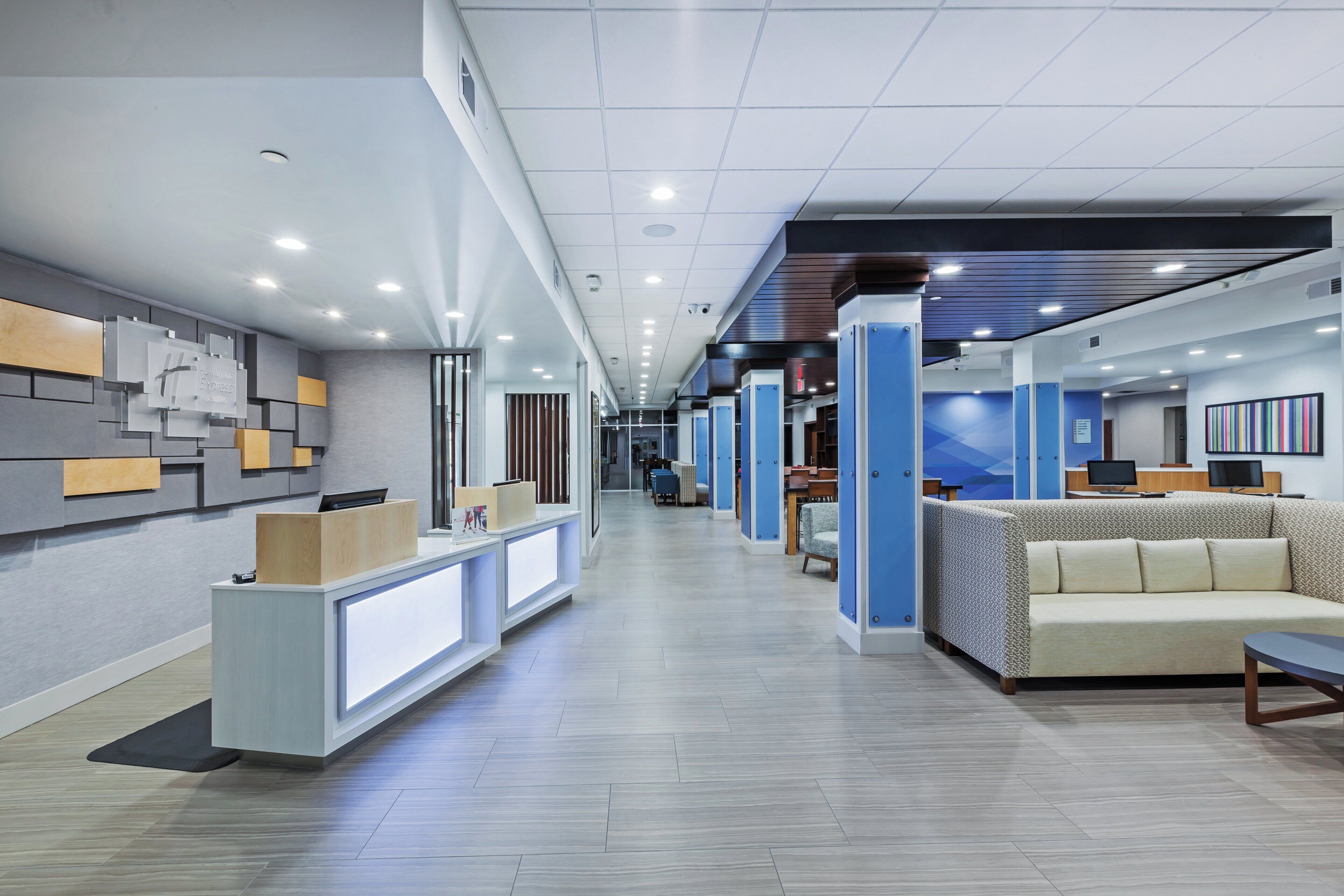 A modern hotel lobby with a reception desk, seating area, and a long corridor leading to other rooms.