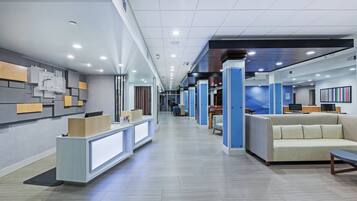 A modern hotel lobby with a reception desk, seating area, and a long corridor leading to other rooms.