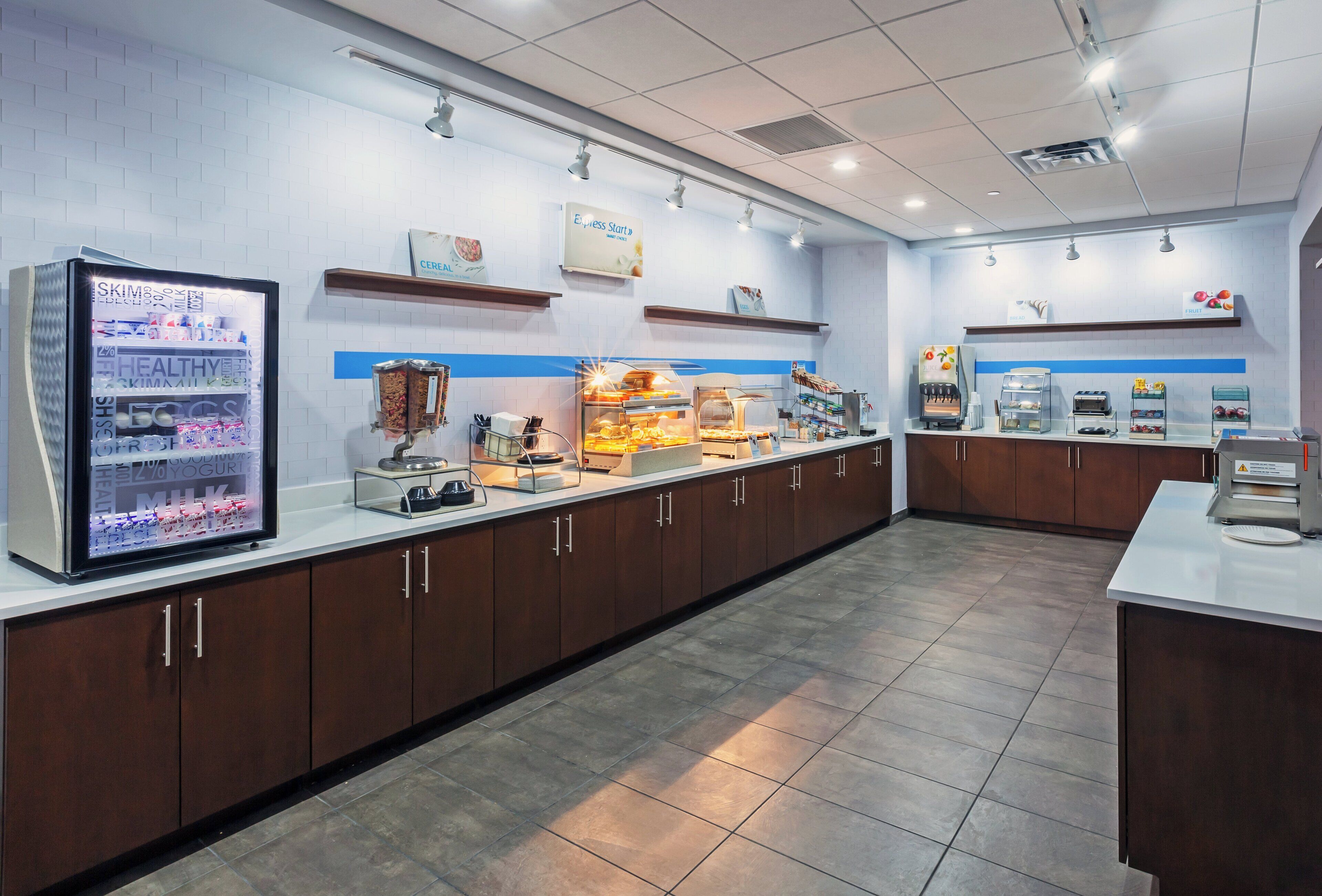 A self-service breakfast area with a refrigerated display, a juice dispenser, and a variety of food options.