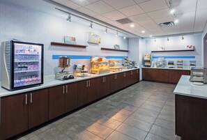 Un espace de petit-déjeuner en libre-service comprenant un présentoir réfrigéré, un distributeur de jus et une variété d'aliments.