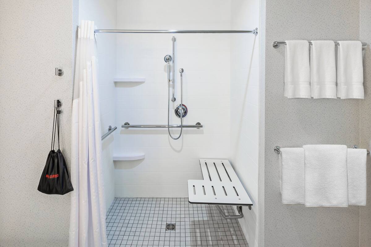 A modern shower area with a grab bar, white tiled walls, and a white towel rack.