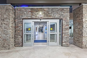 A hotel entrance with a stone facade, automatic doors, and a blue carpet leading inside. - Holiday Inn Express & Suites Coffeyville by IHG (Coffeyville)