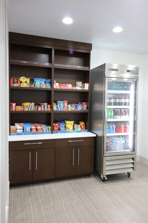 A kitchenette with a refrigerator stocked with beverages and snacks, and a pantry with various food items.