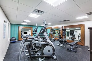 Une salle de sport équipée de divers appareils d’exercice, dotée d’un mur avec des miroirs et d’une enseigne indiquant qu’il s’agit d’un centre de remise en forme.