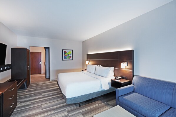 A hotel room with a large bed, a sofa, a desk with a lamp, and a TV.