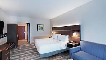 Una habitación de hotel con una cama, un escritorio, una silla, un televisor y un cuadro en la pared.