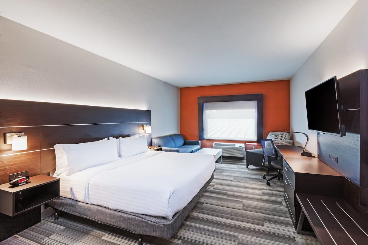A hotel room with a large bed, a desk, a chair, a TV, and a window.