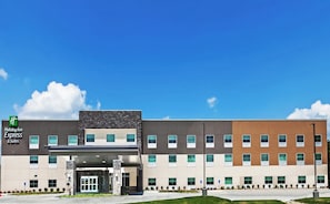 Un hôtel Holiday Inn Express & Suites au design moderne, avec une façade combinant des éléments en pierre et des panneaux, de nombreuses fenêtres et une vue dégagée sur le ciel.