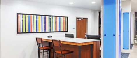 A modern office space with a wooden desk, two chairs, a colorful abstract painting, and a blue storage cabinet.