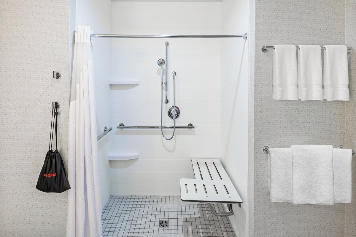 A modern shower area with a grab bar, white tiled walls, and a white towel rack.