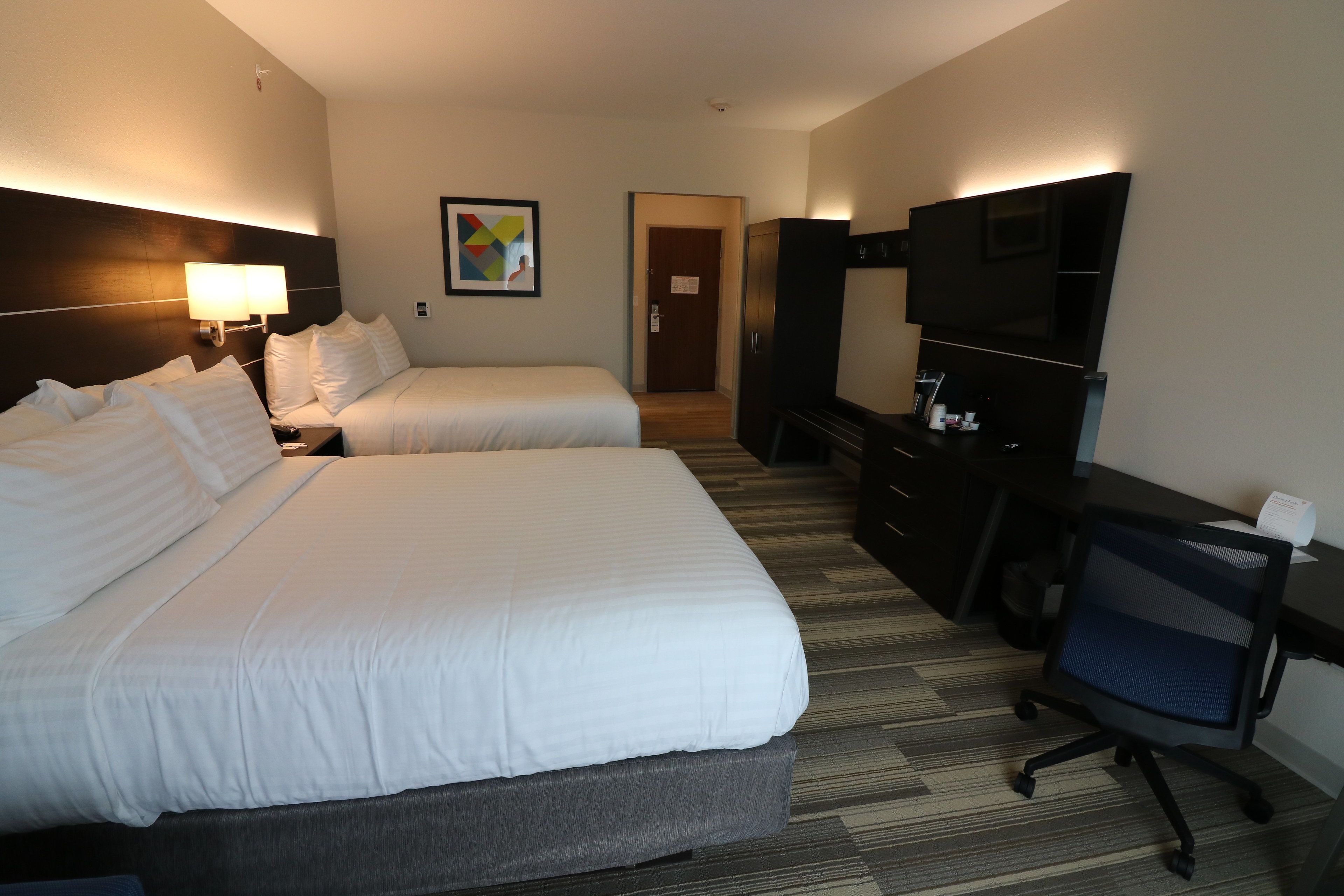 A hotel room with two beds, a desk, a chair, a TV, and a painting on the wall.